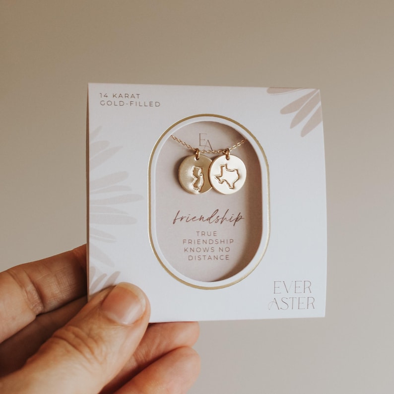May include: A gold-filled necklace with two pendant charms, one shaped like the state of New Jersey and the other like Texas, presented on a white card. The card reads "friendship" and "true friendship knows no distance."