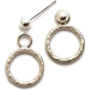 May include: A pair of silver earrings with a hammered texture. One earring features a single circle, while the other has a smaller circle on top of a larger circle.