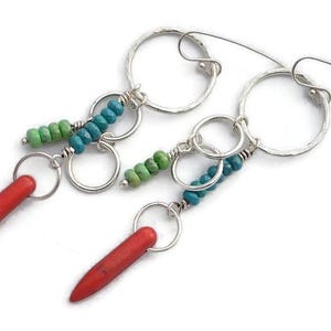 May include: A pair of handcrafted earrings with a unique design. The earrings feature silver hoops, turquoise and green beads, and red, bullet-shaped pendants. The earrings are designed to dangle and catch the light.