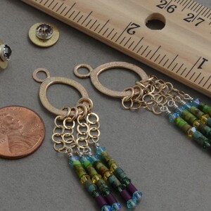 May include: A pair of gold dangle earrings with a circle charm and a chain tassel. The tassel is adorned with green, blue, and purple beads.