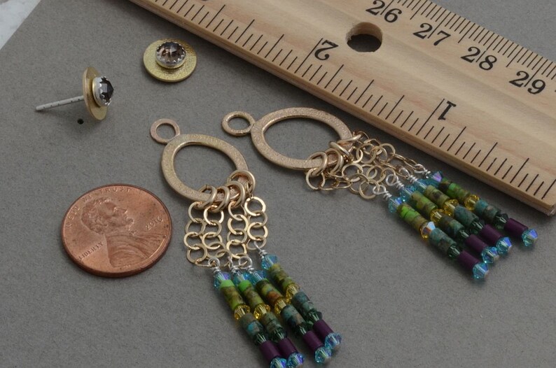 May include: A pair of gold dangle earrings with a circle charm and a chain tassel. The tassel is adorned with green, blue, and purple beads.