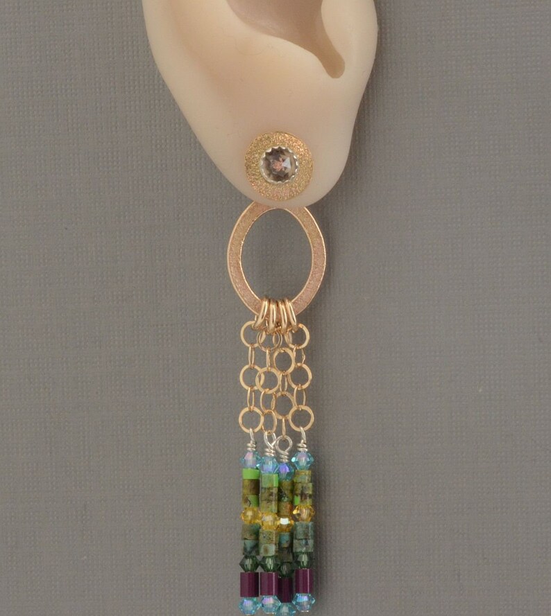 May include: Gold dangle earrings with a small round gemstone at the top, a gold ring, and a chain of gold rings with a multi-colored beaded fringe.