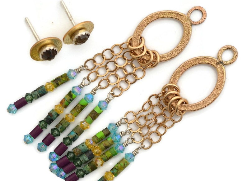 May include: A pair of gold oval earrings with a dangling chain and colorful beads. The beads are in shades of green, blue, purple, and yellow.