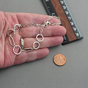 May include: A silver-toned bracelet with a mix of round and oval links, and a matching ring. A ruler with inch measurements is next to the bracelet. A penny is also in the image.