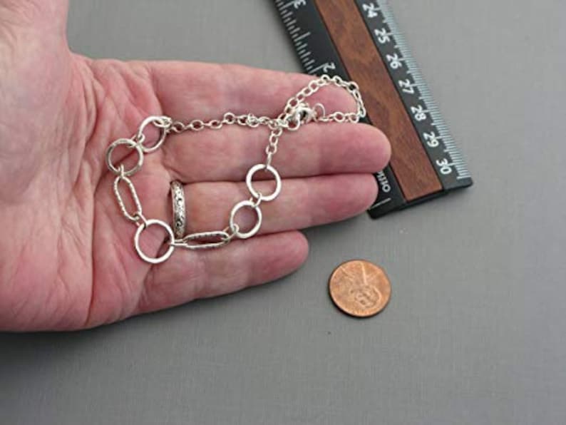 May include: A silver-toned bracelet with a mix of round and oval links, and a matching ring. A ruler with inch measurements is next to the bracelet. A penny is also in the image.