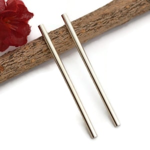 May include: A pair of long, silver earrings. The earrings are thin and straight, and they are hanging from a wooden surface.