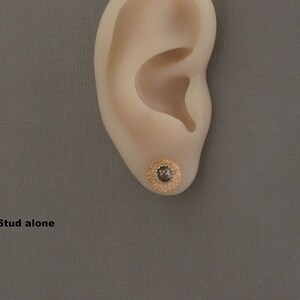 May include: A close-up of a gold stud earring with a small, clear gemstone in the center. The earring is worn in a person's earlobe. The text "Stud alone" is visible below the ear.