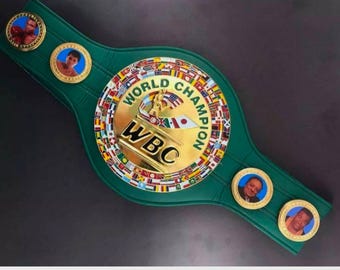 Könnte beinhalten: Ein grüner Gürtel der World Boxing Council (WBC) Meisterschaft. Der Gürtel hat eine goldene Mittelplatte mit den Worten "WORLD CHAMPION" und "WBC". Er hat mehrere kleinere Medaillons mit Porträts von Boxern.
