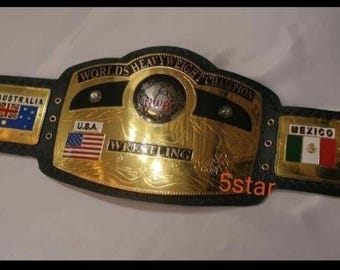 Może przedstawiać: Złoty i czarny pas mistrzowski w zapasach z napisami "WORLD'S HEAVYWEIGHT CHAMPION" i "WRESTLING". Pas zawiera flagi Kanady, Australii, USA, Meksyku i Japonii.