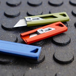 May include: Three utility knives in green, red, and blue. The green knife has its blade extended, while the red knife has its blade retracted. The blue knife is closed. All three knives have a gray slider and a silver blade.
