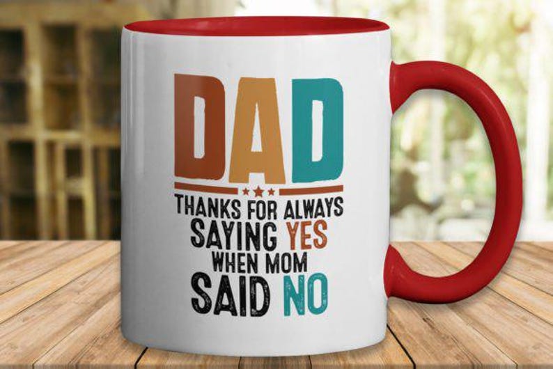 May include: White ceramic mug with a red interior and handle. The mug features the word "DAD" in brown and teal block letters, with the text "THANKS FOR ALWAYS SAYING YES WHEN MOM SAID NO."