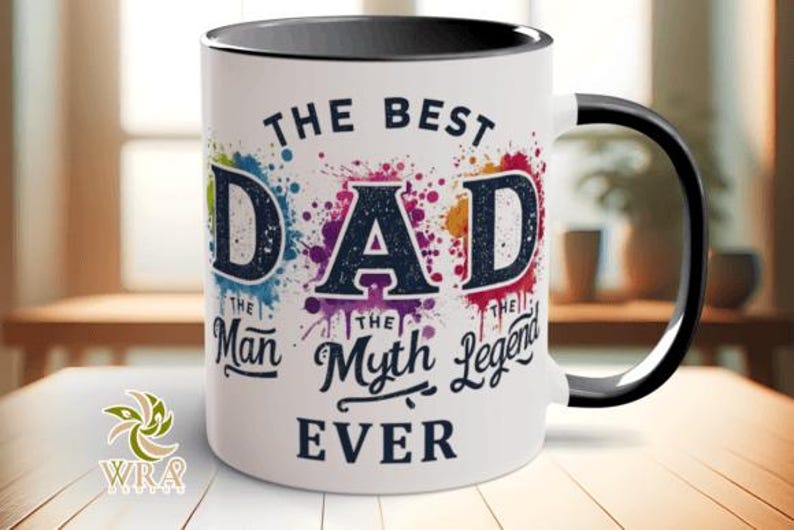 May include: White ceramic mug with a black handle and rim. The mug features the text "THE BEST DAD" in a bold font, with colorful paint splatter accents. Below the text are the words "The Man, The Myth, The Legend, EVER."