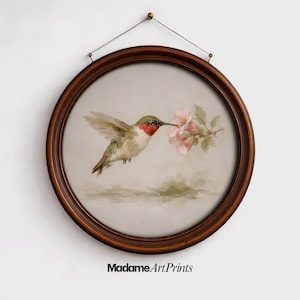 May include: A watercolor painting of a hummingbird feeding from pink flowers, set within a round, dark brown wooden frame. The bird has green, red, and white feathers. The artwork is suspended by a thin wire.