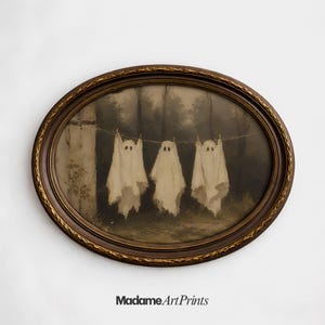 May include: An oval-shaped dark brown frame with gold detailing surrounds a print depicting three white ghost figures hanging from a clothesline against a dark, muted forest background. The text Madame ArtPrints is printed below the frame.