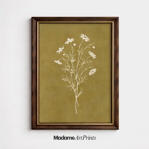 May include: A framed art print featuring a white botanical illustration of daisies on an olive green background. The print is in a dark brown wooden frame with a gold inner border. The text "MadameArtPrints" is at the bottom.