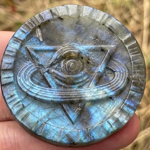 May include: A round, blue-green labradorite stone pendant with a carved eye inside a triangle and a ring around it.