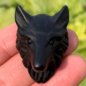 May include: Black obsidian wolf head carving. The wolf's eyes are carved with detail and the fur is textured.