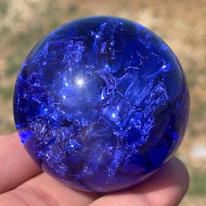 Peut inclure: Une sphère en verre bleu avec un motif marbré tourbillonnant. La sphère est translucide et a une finition brillante.