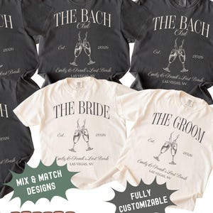 May include: A collection of charcoal gray and ivory t-shirts featuring white graphic prints. The designs include text reading THE BACH CLUB, THE BRIDE, or THE GROOM, along with illustrations of clinking champagne flutes, the text Est. 2026, and Emily & Frank's Last Bash Las Vegas, NV.