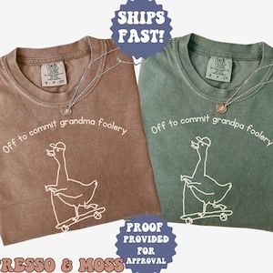 May include: Two t-shirts, one espresso brown and one moss green, each with a white graphic of a goose on a skateboard and the phrase "Off to commit grandma/pa foolery." Both shirts have a necklace.