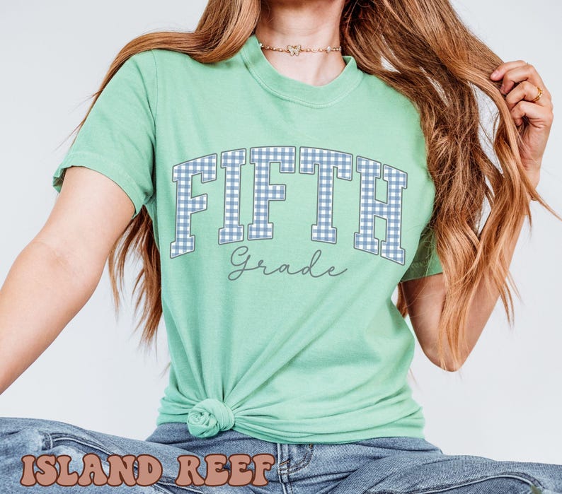 May include: A light green short-sleeve t-shirt featuring the word FIFTH in a blue and white gingham pattern with a dark outline, and the word Grade written in a cursive script font below it. The shirt is tied in a knot at the bottom hem.
