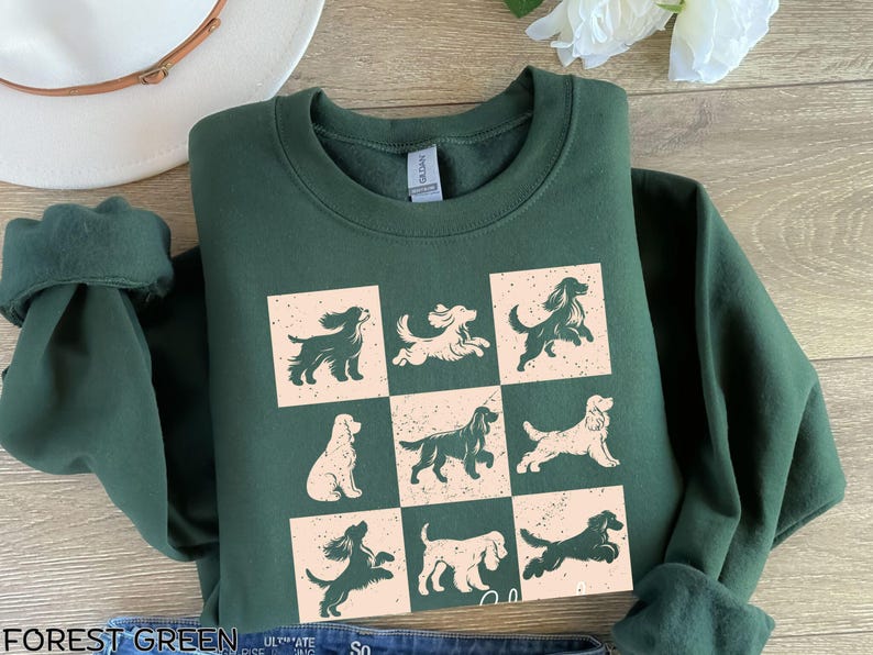 May include: Forest green sweatshirt featuring a grid of nine dog illustrations in various poses. The dogs are in a distressed, vintage style, with a mix of dark green and cream colors. The sweatshirt has a crew neck and long sleeves.