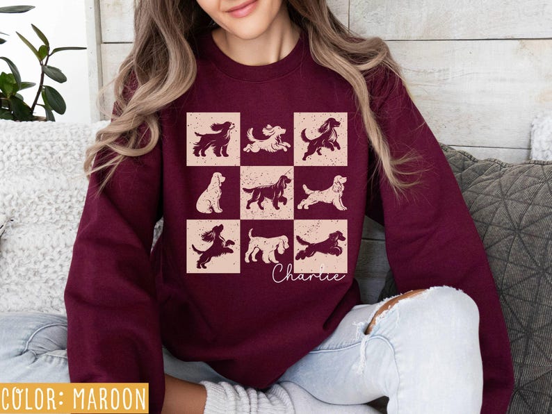 May include: Maroon sweatshirt featuring a grid of dog illustrations in various poses. The design includes the name "Charlie" in cursive. The sweatshirt is a solid maroon color, with a distressed, vintage-style graphic.