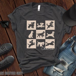 May include: Dark heather grey t-shirt featuring a grid of nine dog illustrations in various poses. The word "Charlie" is written in cursive below the grid. The shirt is paired with sunglasses, sneakers, a baseball cap, and jeans.