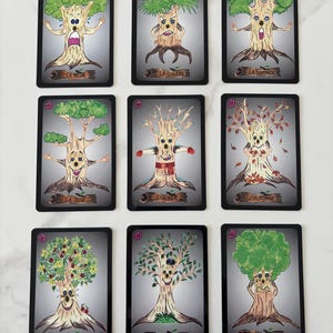 May include: Nine illustrated cards featuring anthropomorphic trees with expressive faces and various emotions. Each card has a black border and a French word at the bottom, such as "La Peur" (Fear) and "La Colère" (Anger). The trees' appearances vary with the seasons.