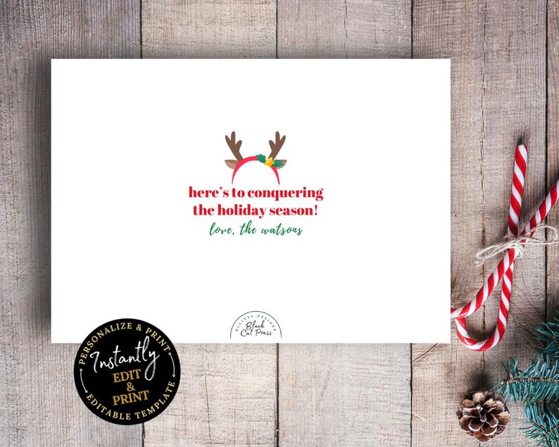 Op de afbeelding: Een witte wenskaart met de tekst "here's to conquering the holiday season!" in het rood en groen. De kaart heeft een rendiergeweimotief en wordt omringd door zuurstokken en dennennaalden.