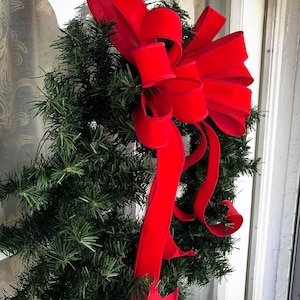 May include: A green Christmas wreath with a large red velvet bow. The wreath is hanging on a white door.