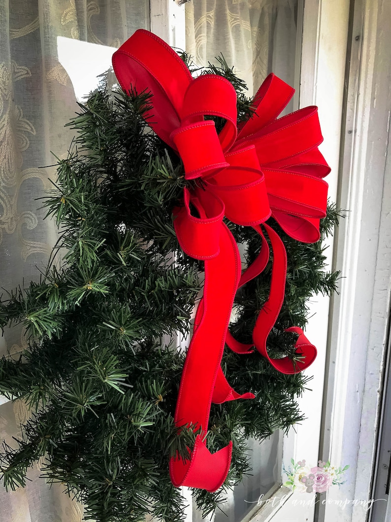 May include: A green Christmas wreath with a large red velvet bow. The wreath is hanging on a white door.