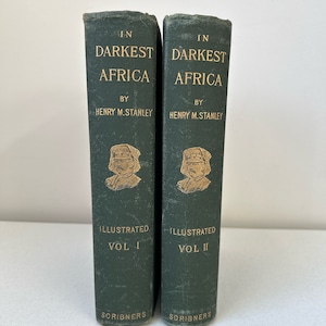 May include: Two vintage books titled "In Darkest Africa" by Henry M. Stanley. The green hardcovers feature gold lettering and illustrations. Volume I and Volume II are displayed side by side, published by Scribners.