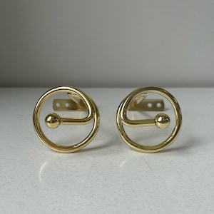 Peut inclure: Deux supports de tringle à rideaux dorés. Chaque support présente un design circulaire avec une petite sphère et un support de montage à trois trous. Les supports sont en métal brillant.