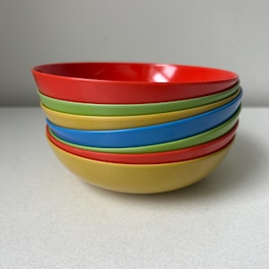 May include: A stack of six round bowls in various solid colors including red, light green, yellow, and blue. The bowls are nested together, creating a layered appearance with smooth, curved edges and a simple, functional design for serving food.