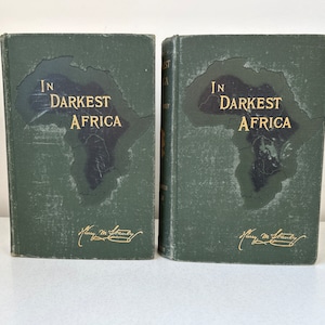 May include: Two vintage books titled "In Darkest Africa" with a map of Africa on the cover. The books have a dark green cover with gold lettering and a signature. The books are displayed side by side.
