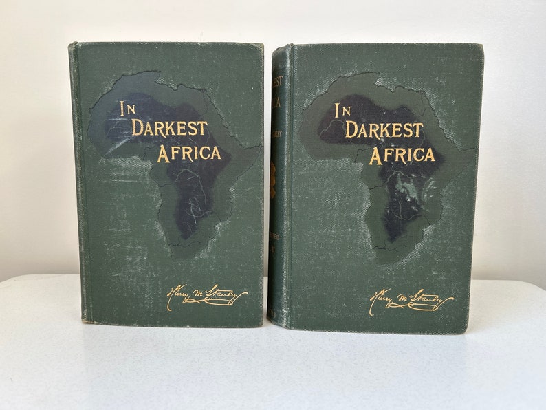 May include: Two vintage books titled "In Darkest Africa" with a map of Africa on the cover. The books have a dark green cover with gold lettering and a signature. The books are displayed side by side.
