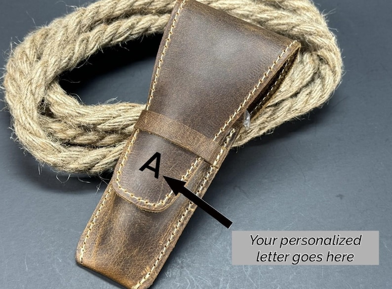 May include: A brown leather case with a stitched edge and a letter "A" embossed on the front. The case is designed to hold a straight razor.