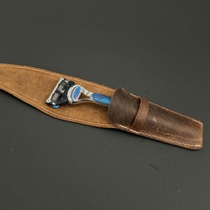 May include: A brown leather razor case with a silver and blue razor inside.