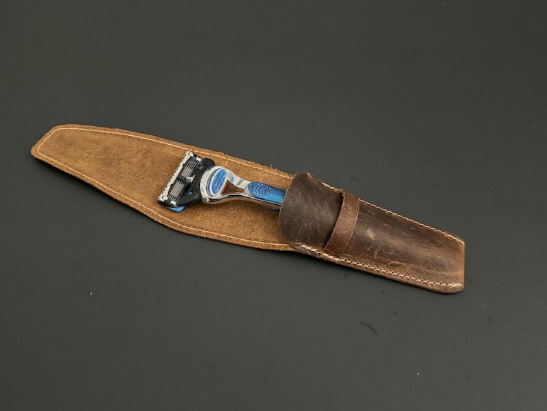 May include: A brown leather razor case with a silver and blue razor inside.