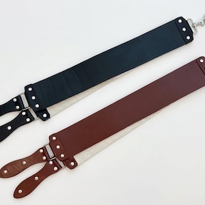 以下が含まれることがあります： 黒と茶色のレザー製カミソリ用ストロップ2本。それぞれ長い長方形のレザーベルトが銀色の金属製リベットでハンドルに取り付けられており、上部には回転フック、裏面には明るい色のキャンバス地が施されています。