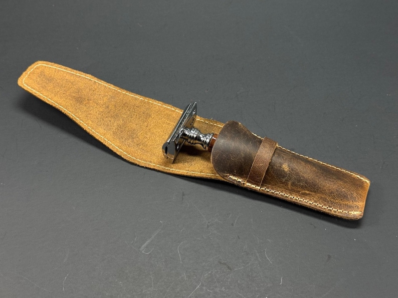 May include: A brown leather case with a stitched edge and a silver and wood safety razor inside.