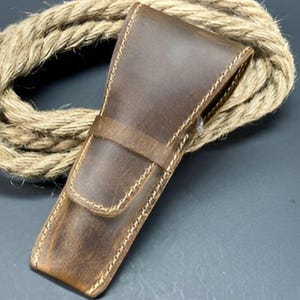 May include: A brown leather case with stitching detail. The case is designed to hold a straight razor.