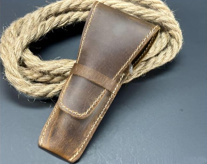 May include: A brown leather case with stitching detail. The case is designed to hold a straight razor.