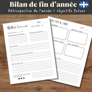 May include: Two white sheets of paper with the text "Bilan de fin d'année" and "Rétrospective de l'année + objectifs futurs" in black. The sheets have lines and boxes for writing. The background is a wooden surface.