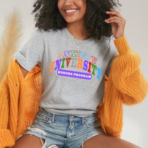 Puede incluir: Una camiseta gris con el texto "Anxiety University Honors Program" en un diseño de arcoíris.
