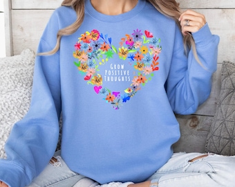 May include: A light blue sweatshirt with a colorful floral heart design and the text "Grow Positive Thoughts".