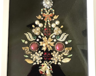 May include: A framed wall art piece featuring a Christmas tree design constructed from various vintage jewelry pieces, including gold-tone brooches, faux pearls, red and green rhinestones, candy cane charms, and bell ornaments on a black background.