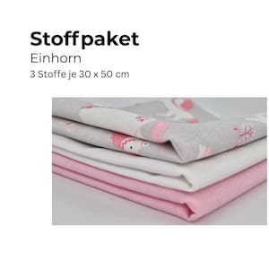 Può includere: Una pila di tre pezzi di tessuto, ciascuno di 30 x 50 cm. Il tessuto superiore è grigio con un motivo a unicorno, quello centrale è bianco e quello inferiore è rosa. Il testo in alto recita "Stoffpaket Einhorn".