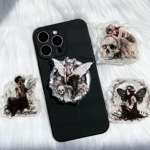May include: Black smartphone with a pop-up phone grip featuring a fairy design with skulls and roses. Three additional fairy-themed acrylic charms are also visible, each with a unique design of fairies and skulls.